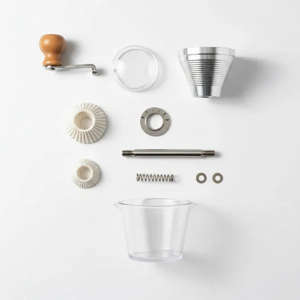 Close-up of a disassembled hand coffee grinder with its key parts laid out on a clean surface.